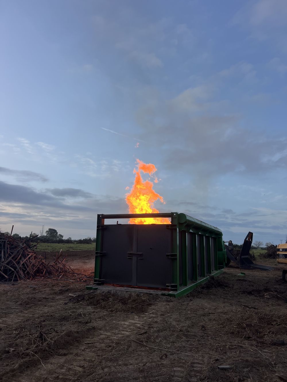 Green air curtain burner with flames rising from the firebox at dusk